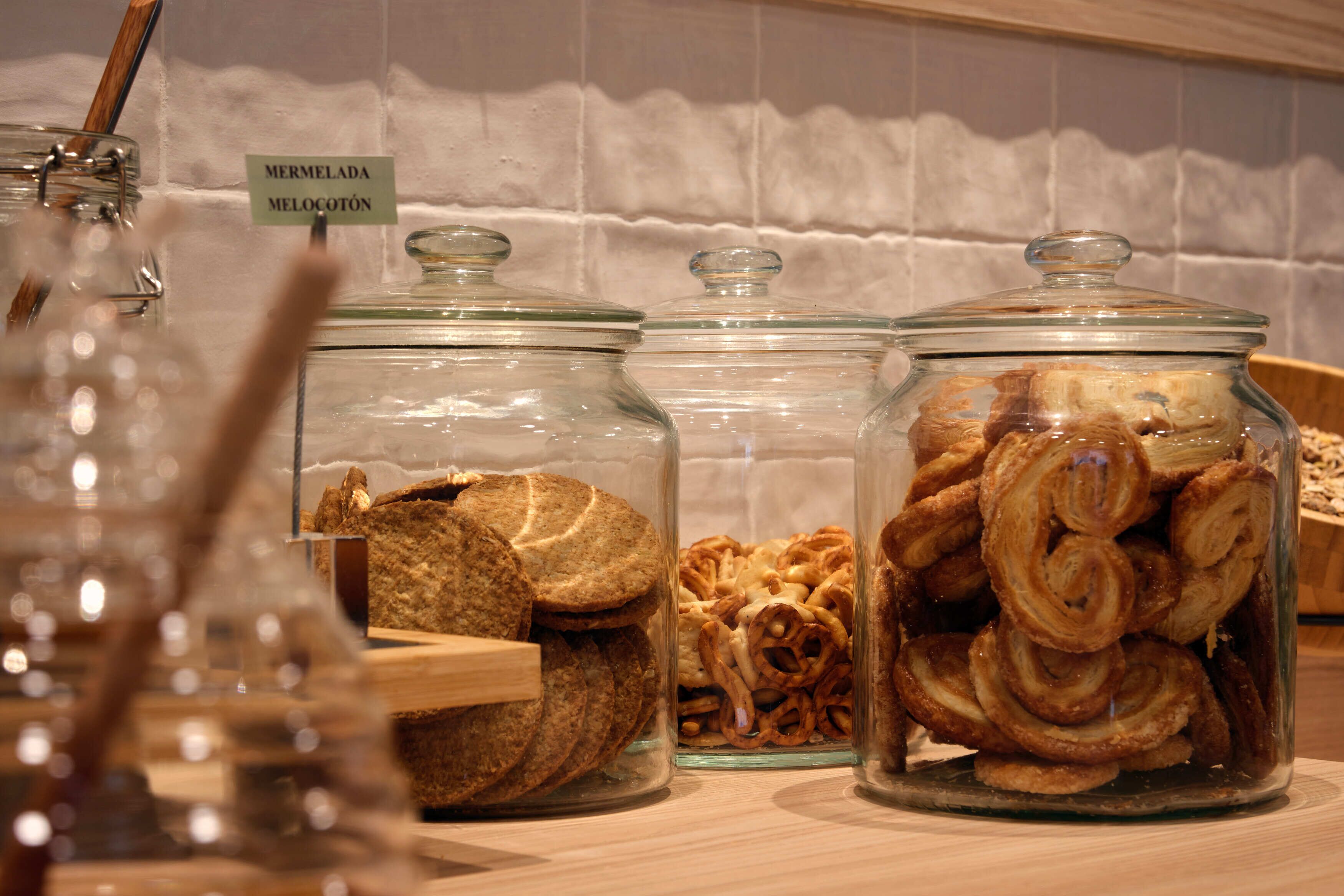 Drei Glaskörbe mit Etiketten auf einer Holztischplatte, gefüllt mit verschiedenen Backwaren.