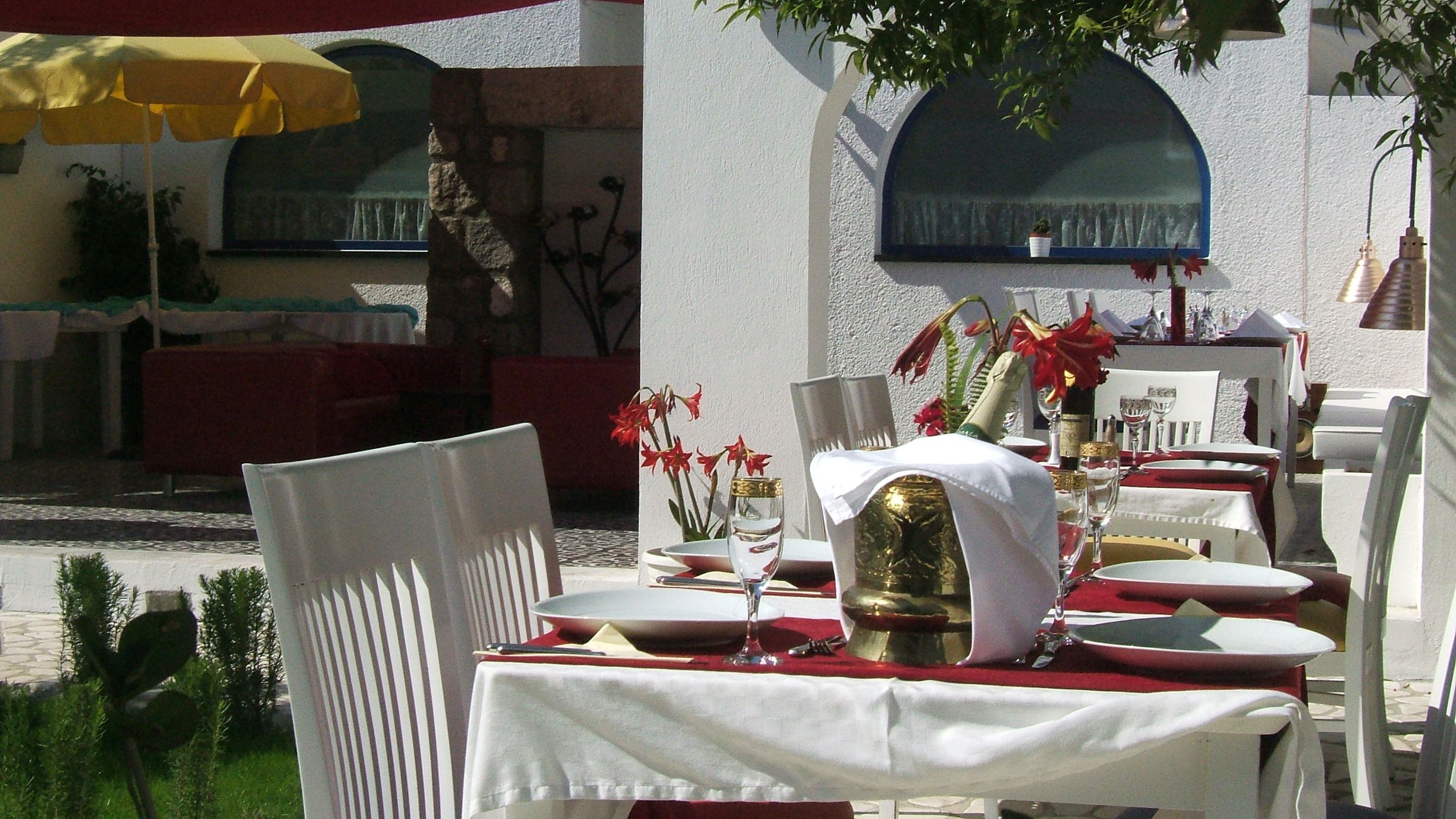 An outdoor dining area with white tables and chairs, red tablecloths, and yellow umbrellas.