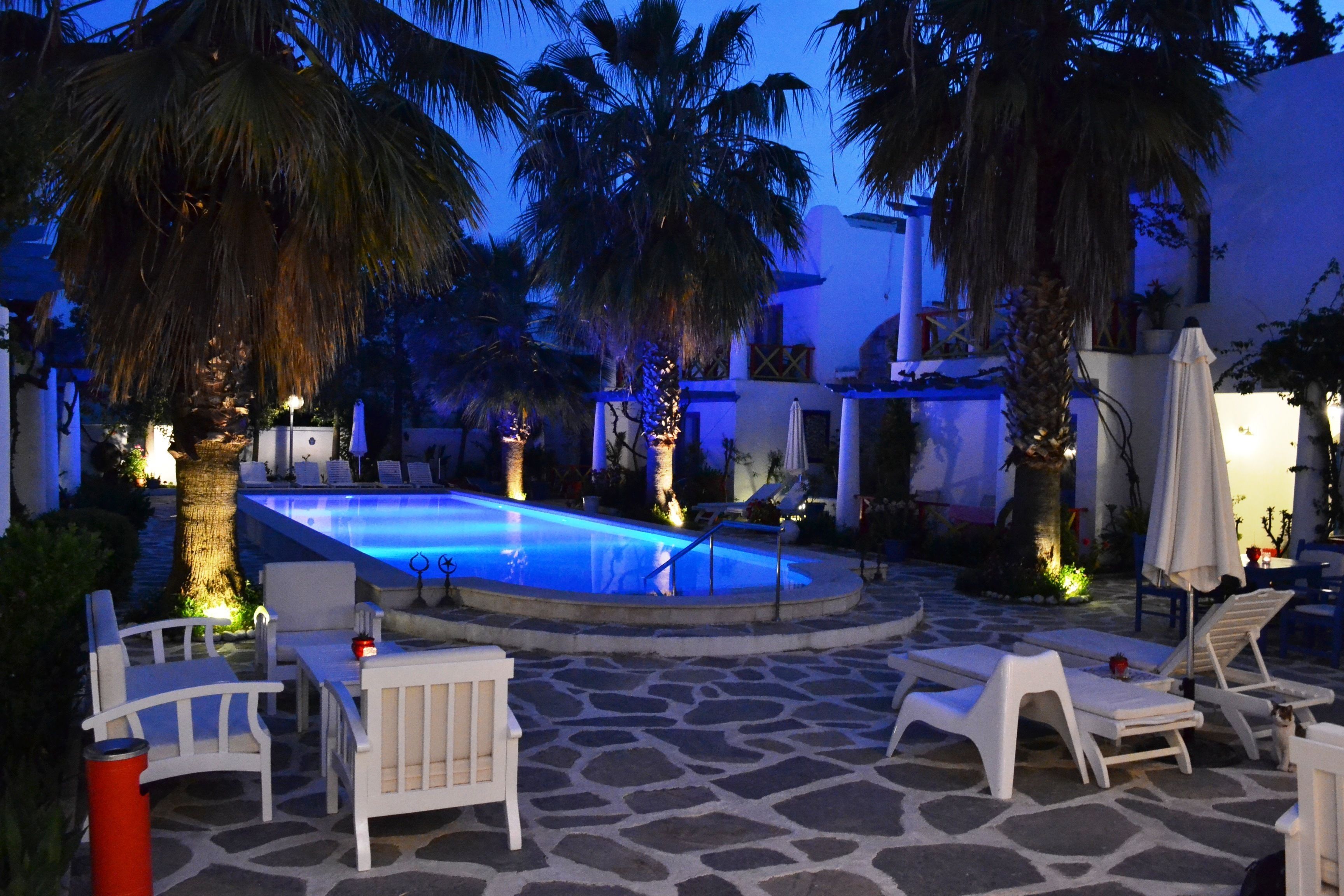 Un espace piscine aménagé avec des chaises longues et une petite table, entouré de palmiers et doté d’un sol en pierre.