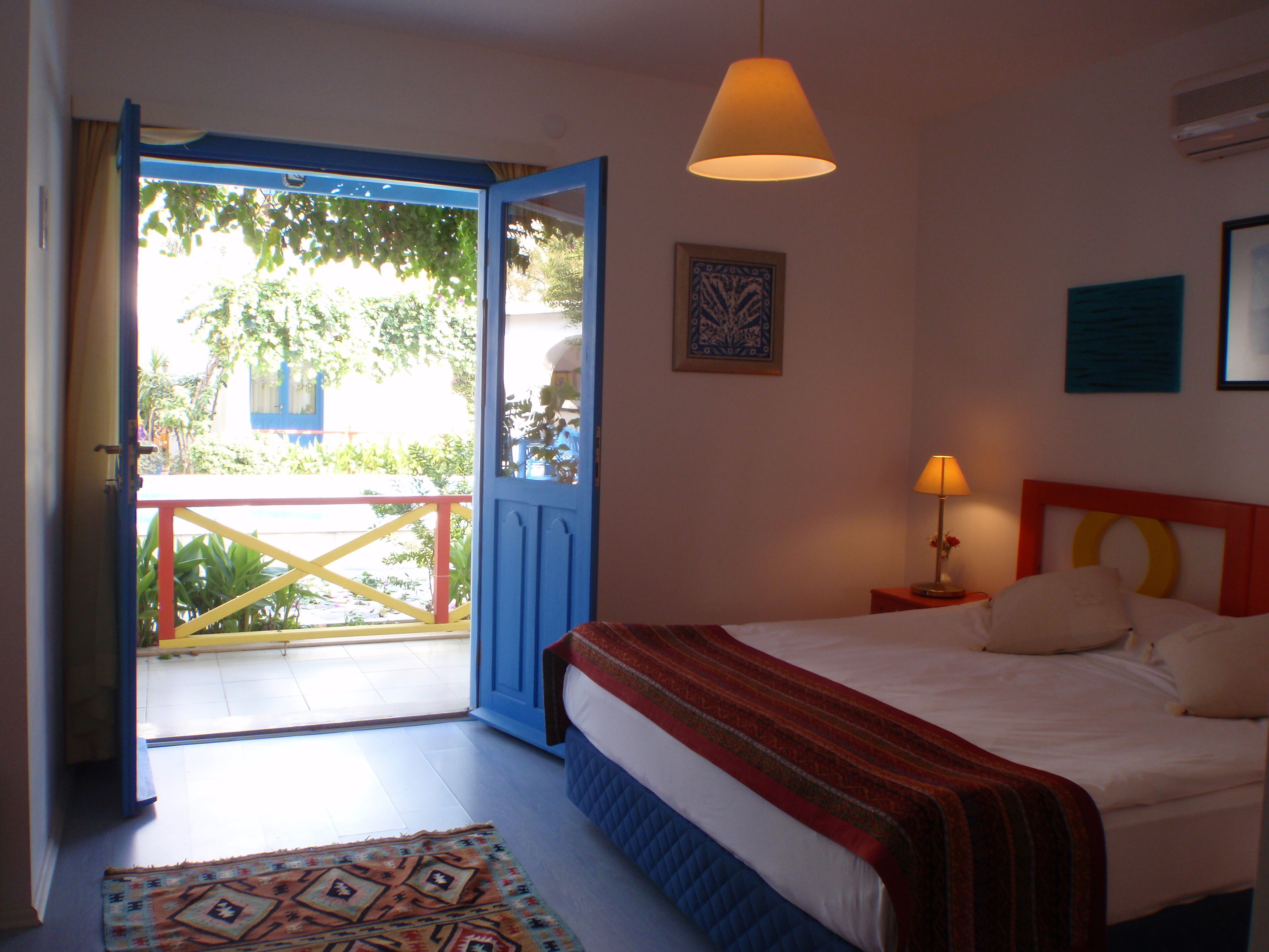 A bedroom with a bed, a nightstand, a lamp, a window with curtains, and a door leading outside.