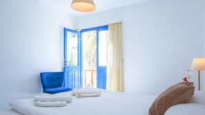 A hotel room with a bed, a blue chair, a window with curtains, and a small table with a lamp. - Su Hotel (Bodrum)