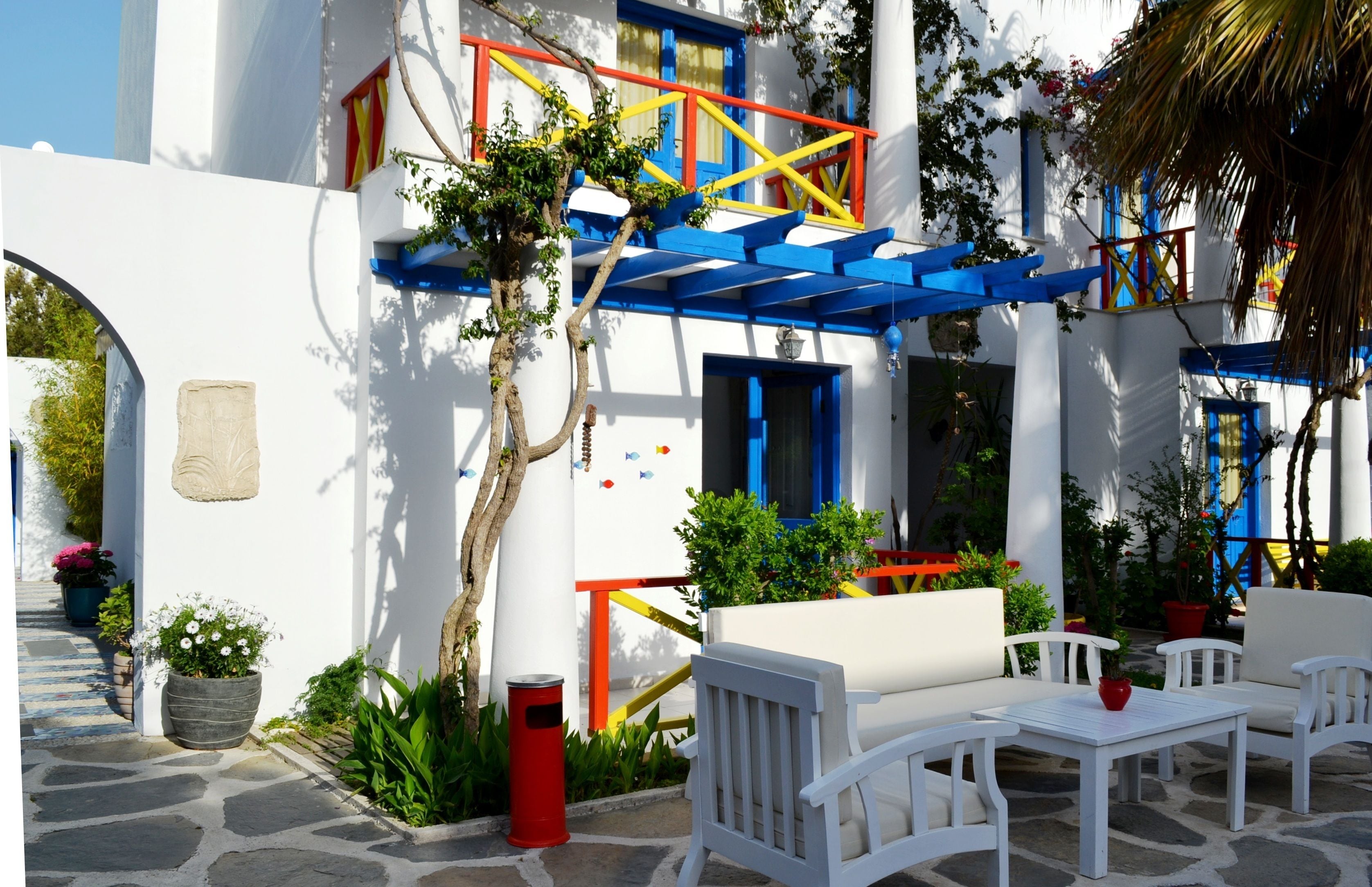 Un edificio blanco con detalles azules, mesas al aire libre y plantas en macetas.