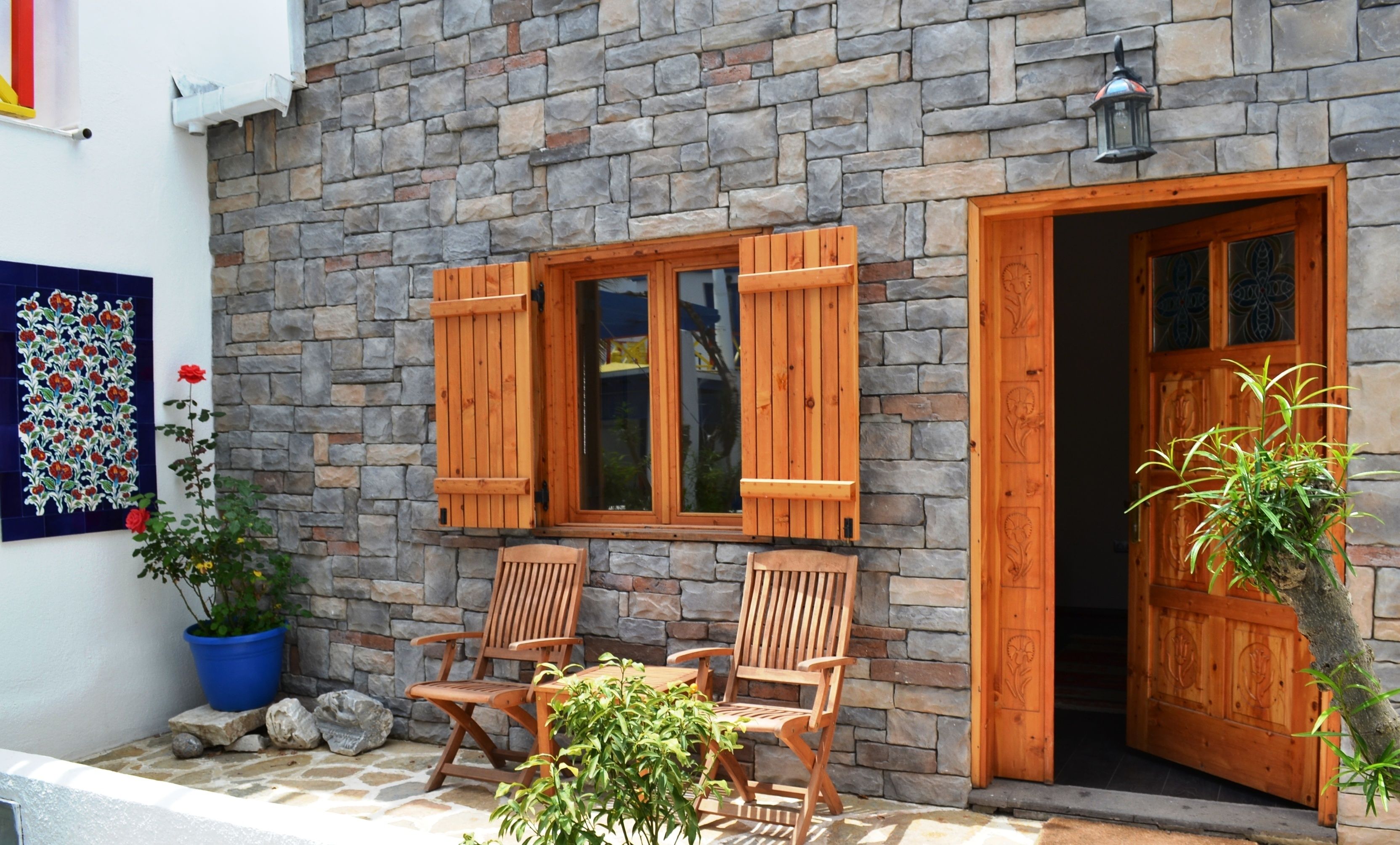 A stone building with a wooden door and windows, two wooden chairs, and a potted plant.