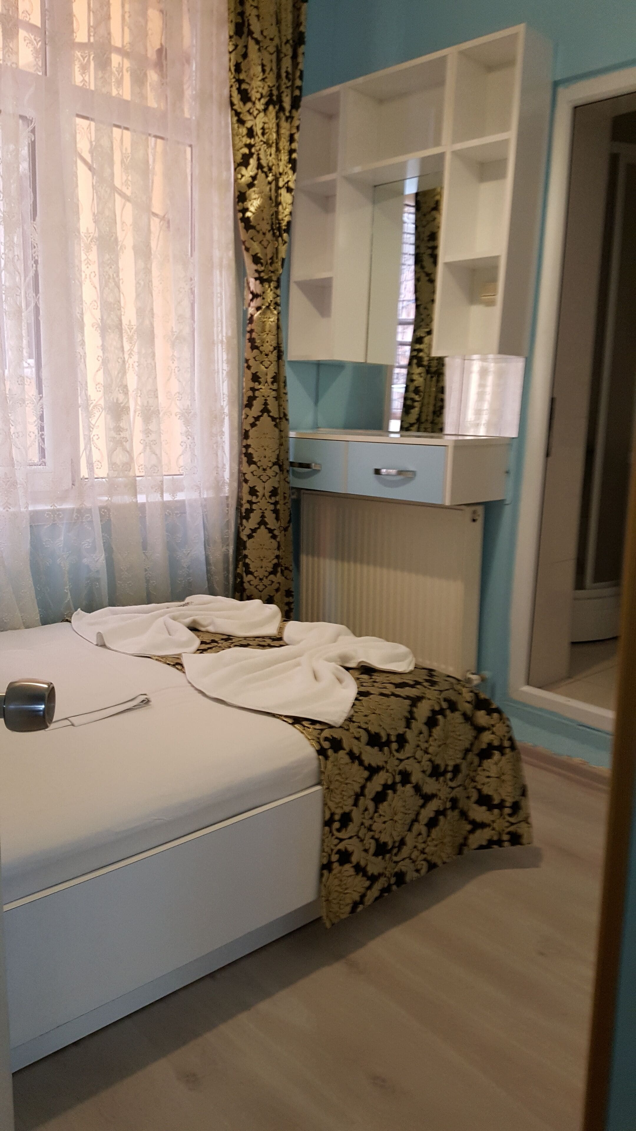 A bedroom with a bed, a bedside table, a mirror, a wardrobe, and a window with curtains.