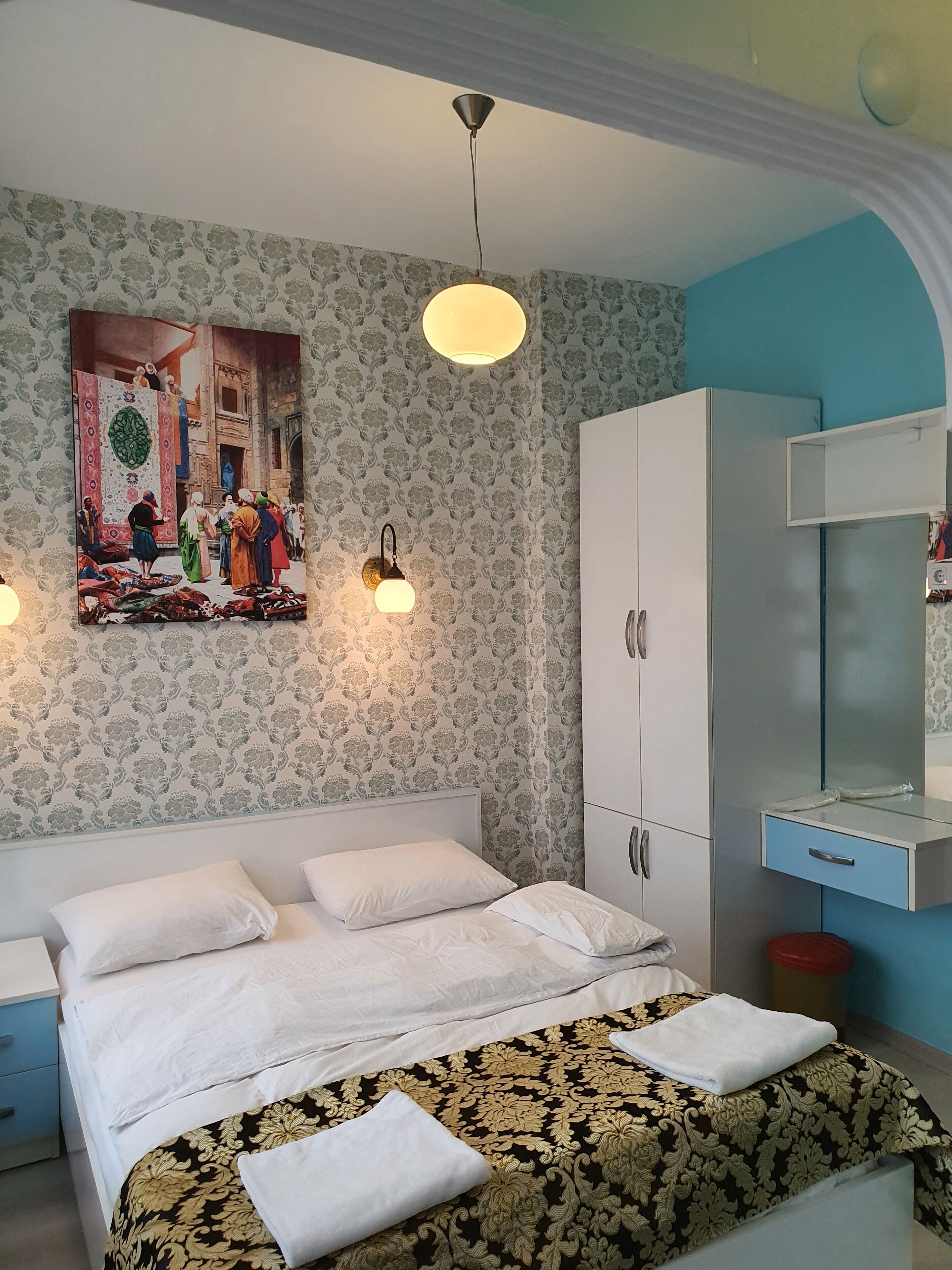 A bedroom with a bed, a wardrobe, a nightstand, and a wall-mounted lamp.