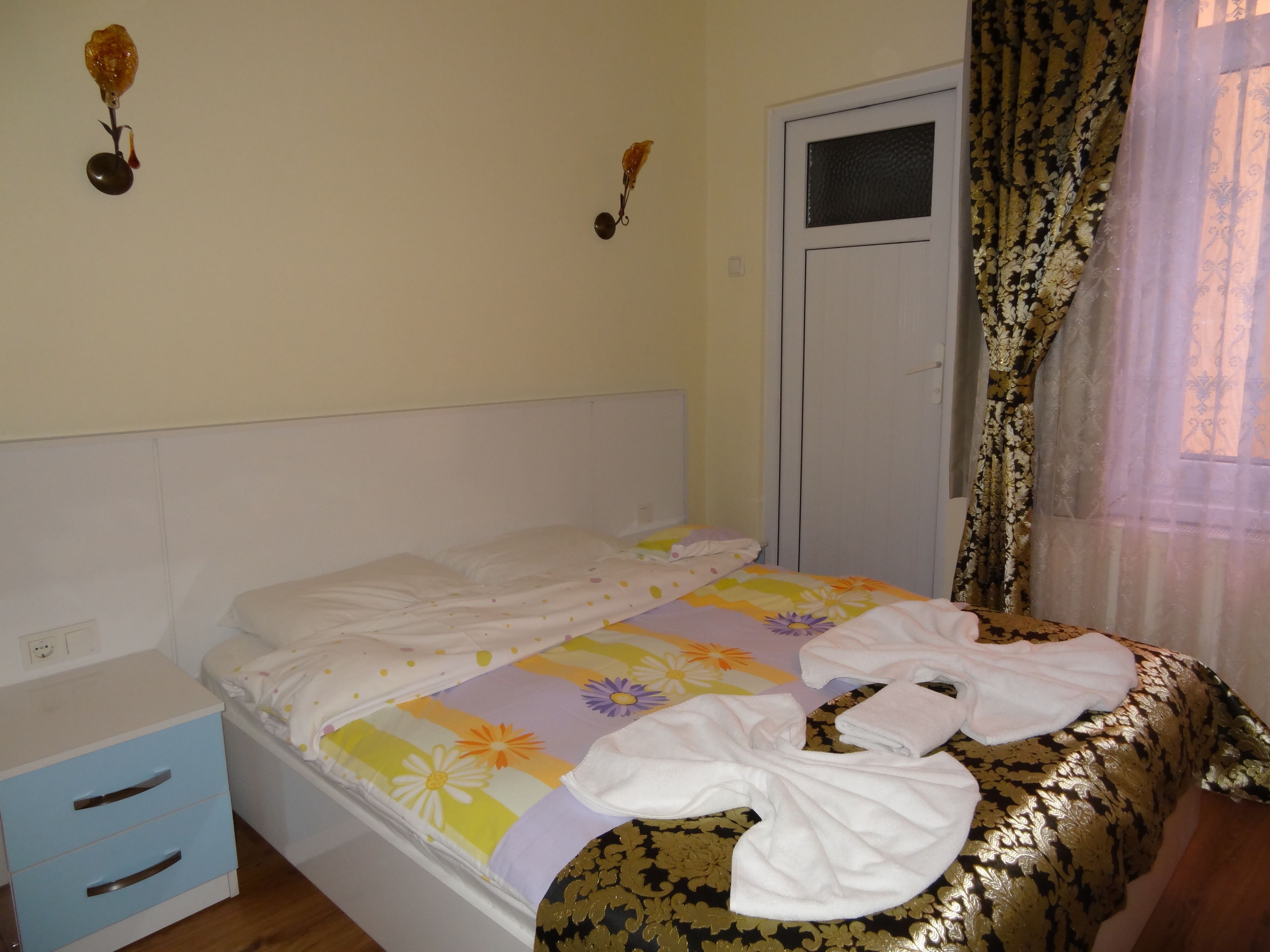 Quarto com cama, mesa de cabeceira, guarda-roupa e janela com cortinas.