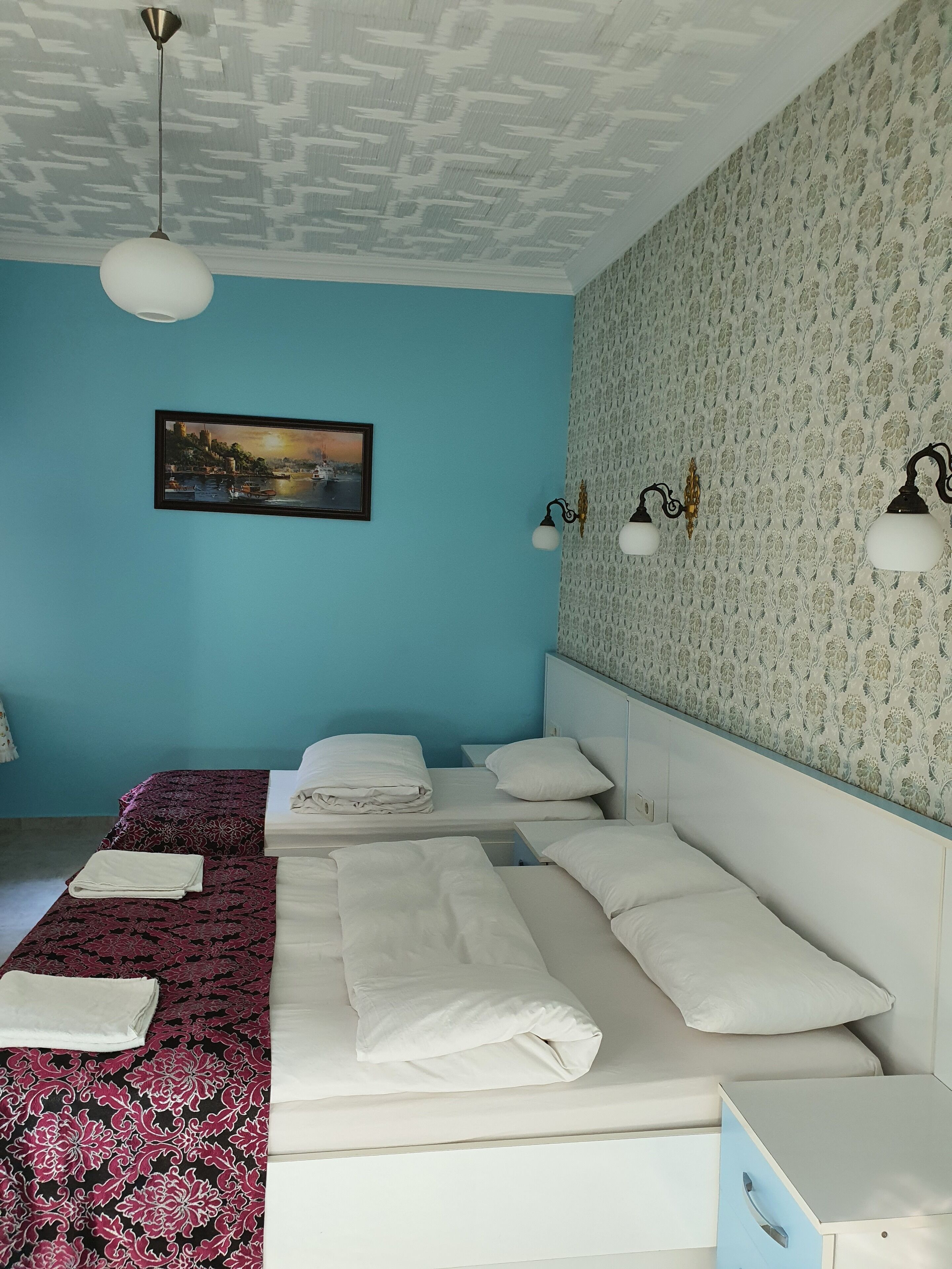 A hotel room with a bed, a nightstand, a wall-mounted lamp, and a framed picture.