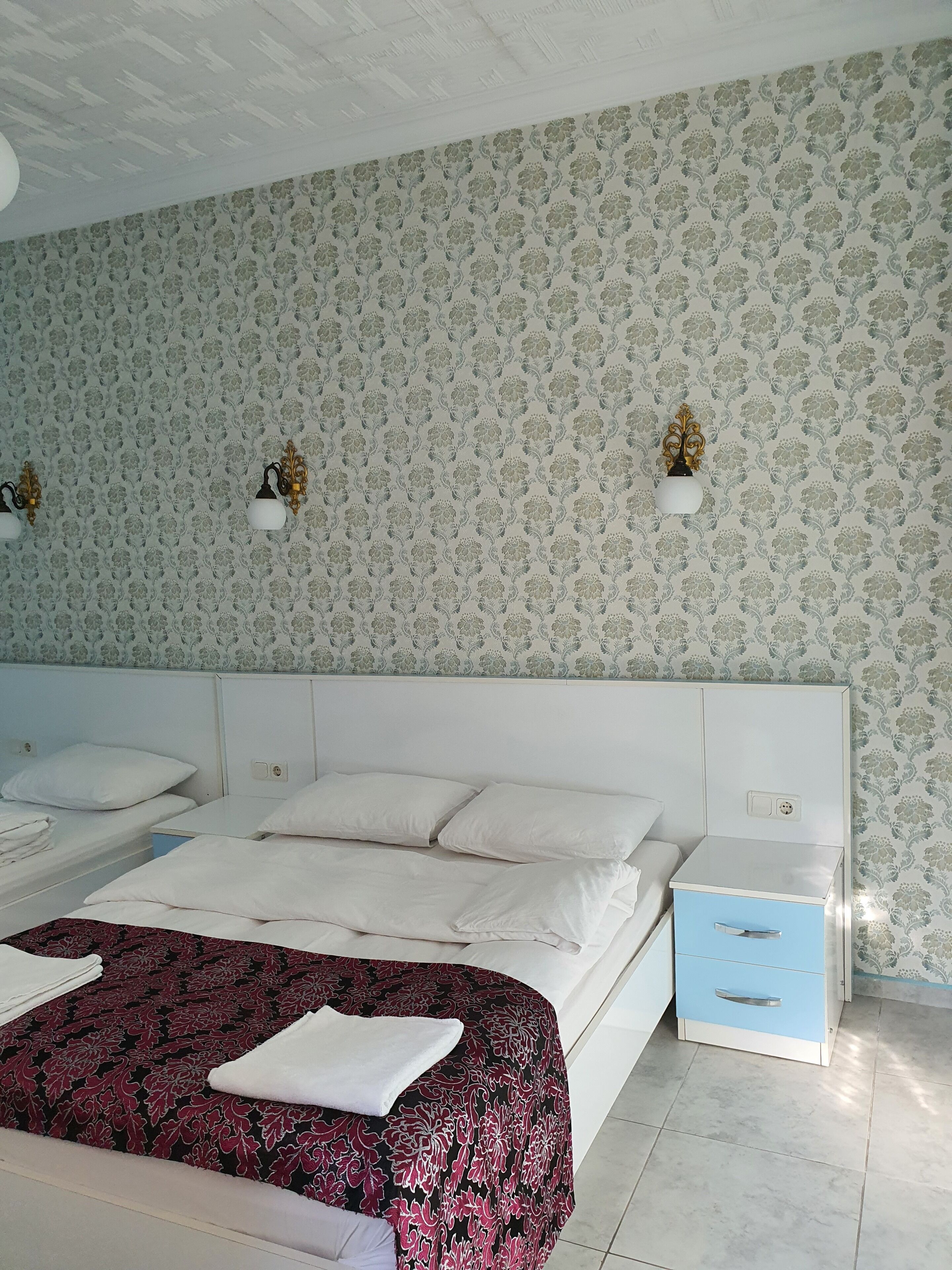 A hotel room with a large bed, two bedside tables, a nightstand, and a blue drawer unit.