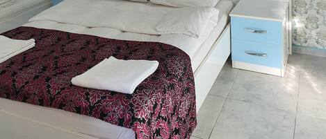 A hotel room with a large bed, two bedside tables, a nightstand, and a blue drawer unit.