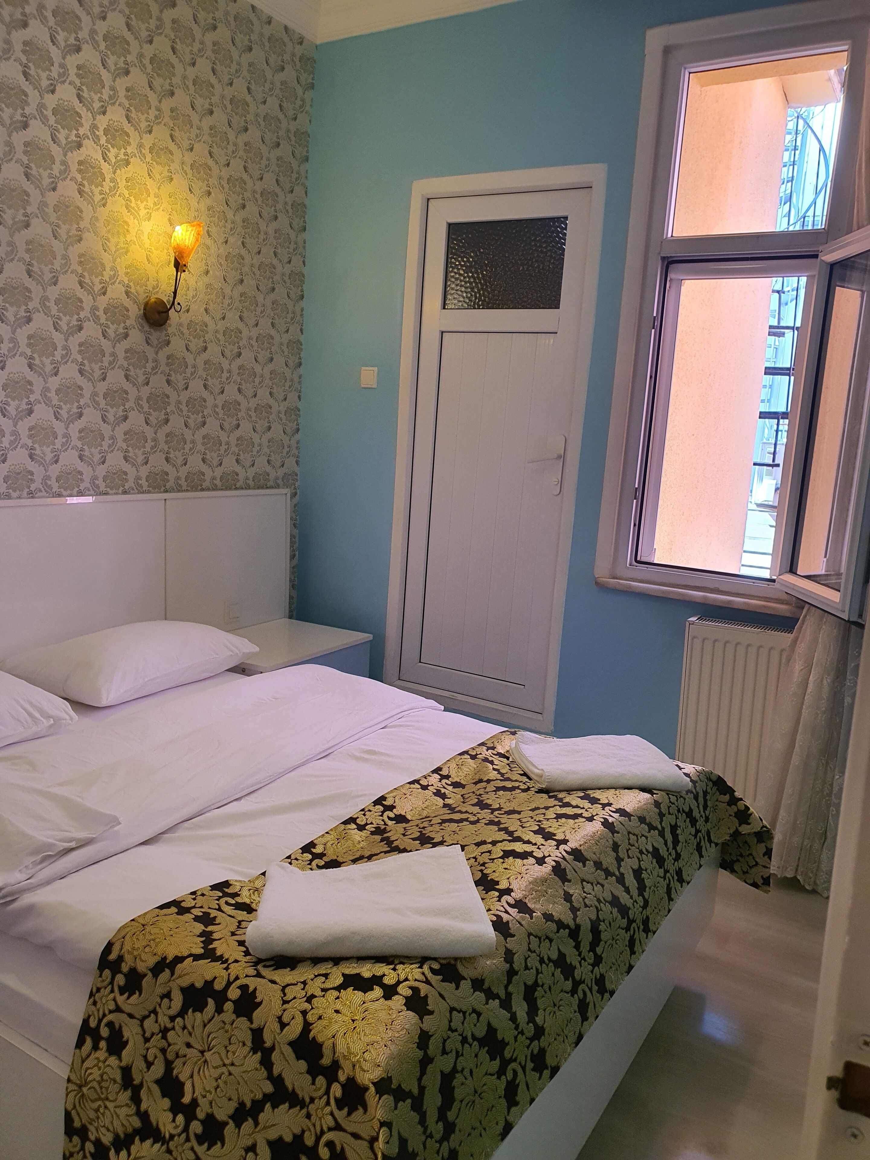 Ein Schlafzimmer mit einem Bett, einem Fenster, einer Tür und einer Wand mit ornamentalem Wandpapier.