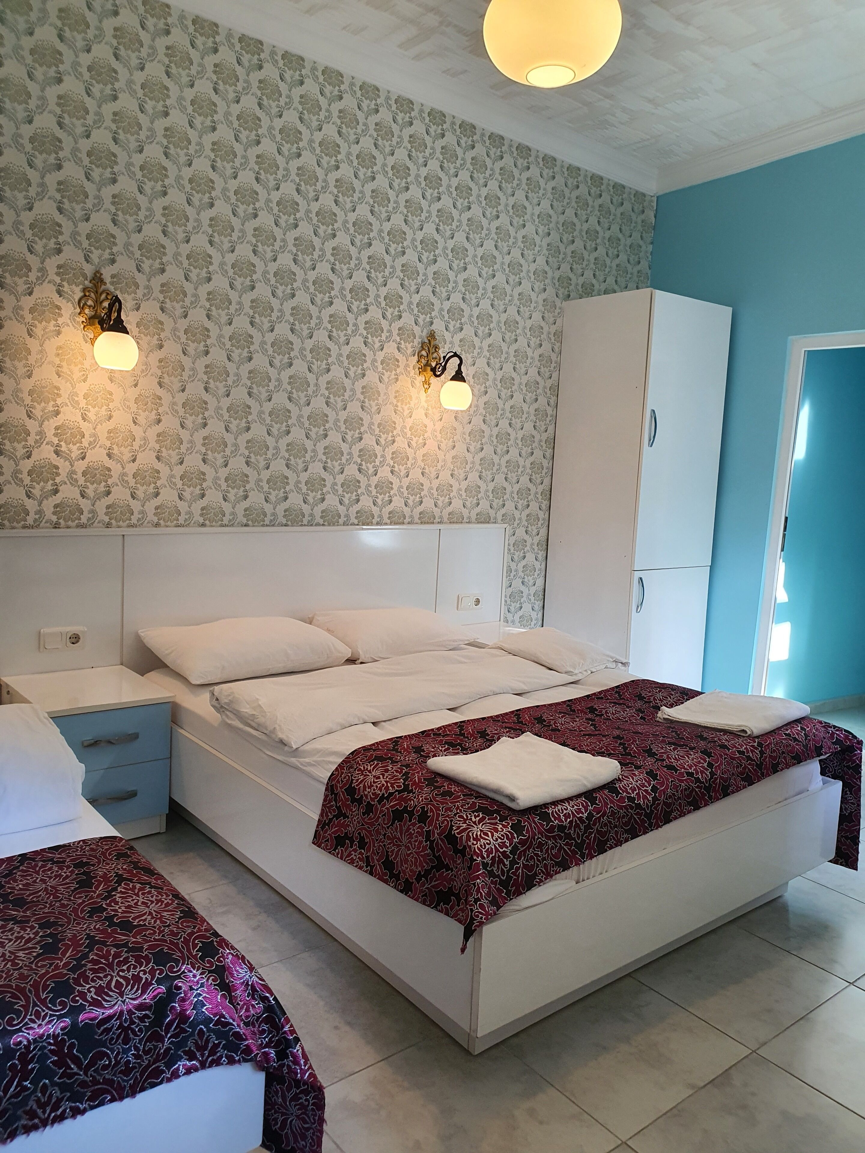 A bedroom with a large bed, a nightstand, a wardrobe, and two wall-mounted lights.