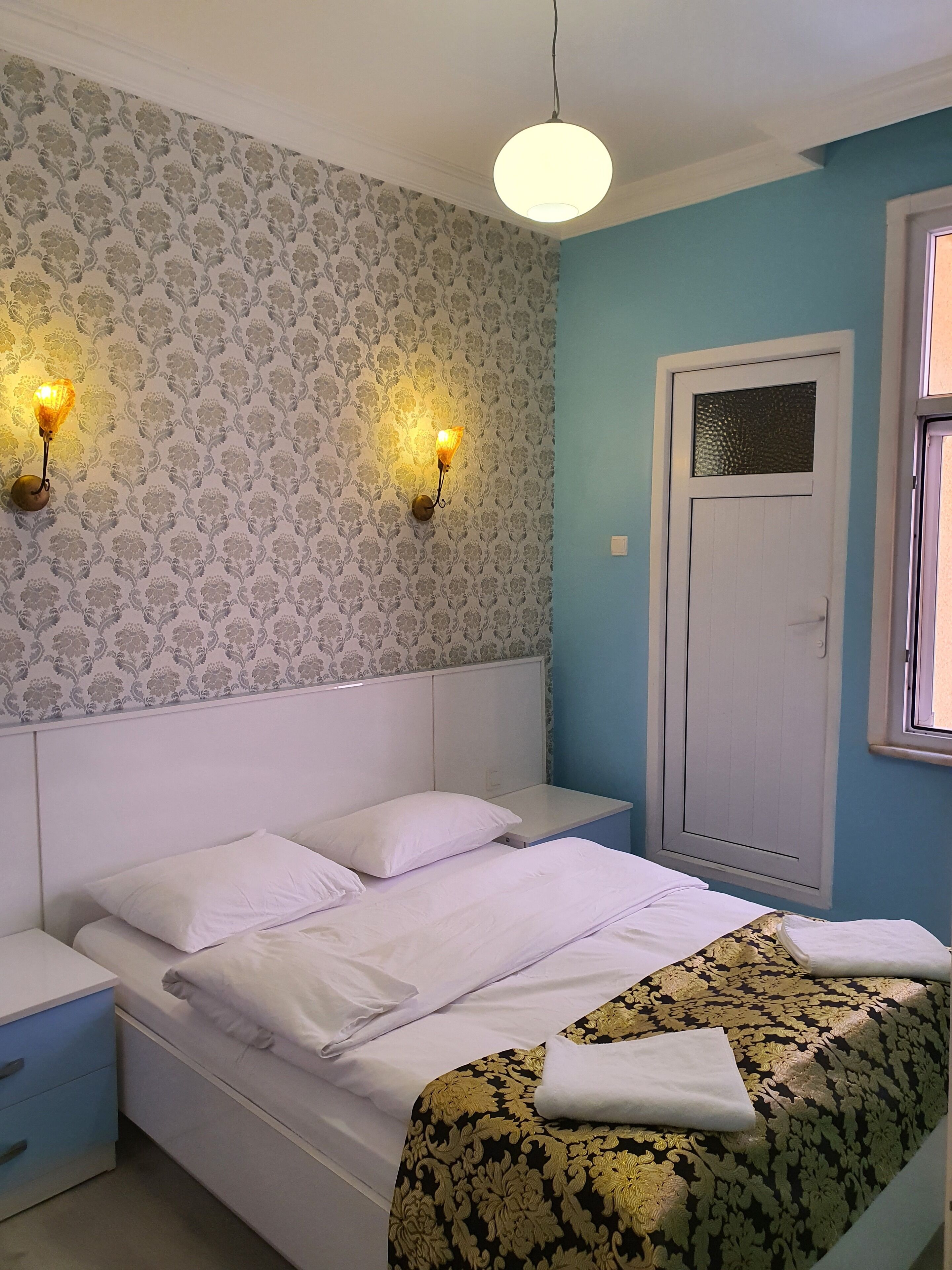 A bedroom with a bed, two bedside tables, a wall-mounted light fixture, and a door with a window.