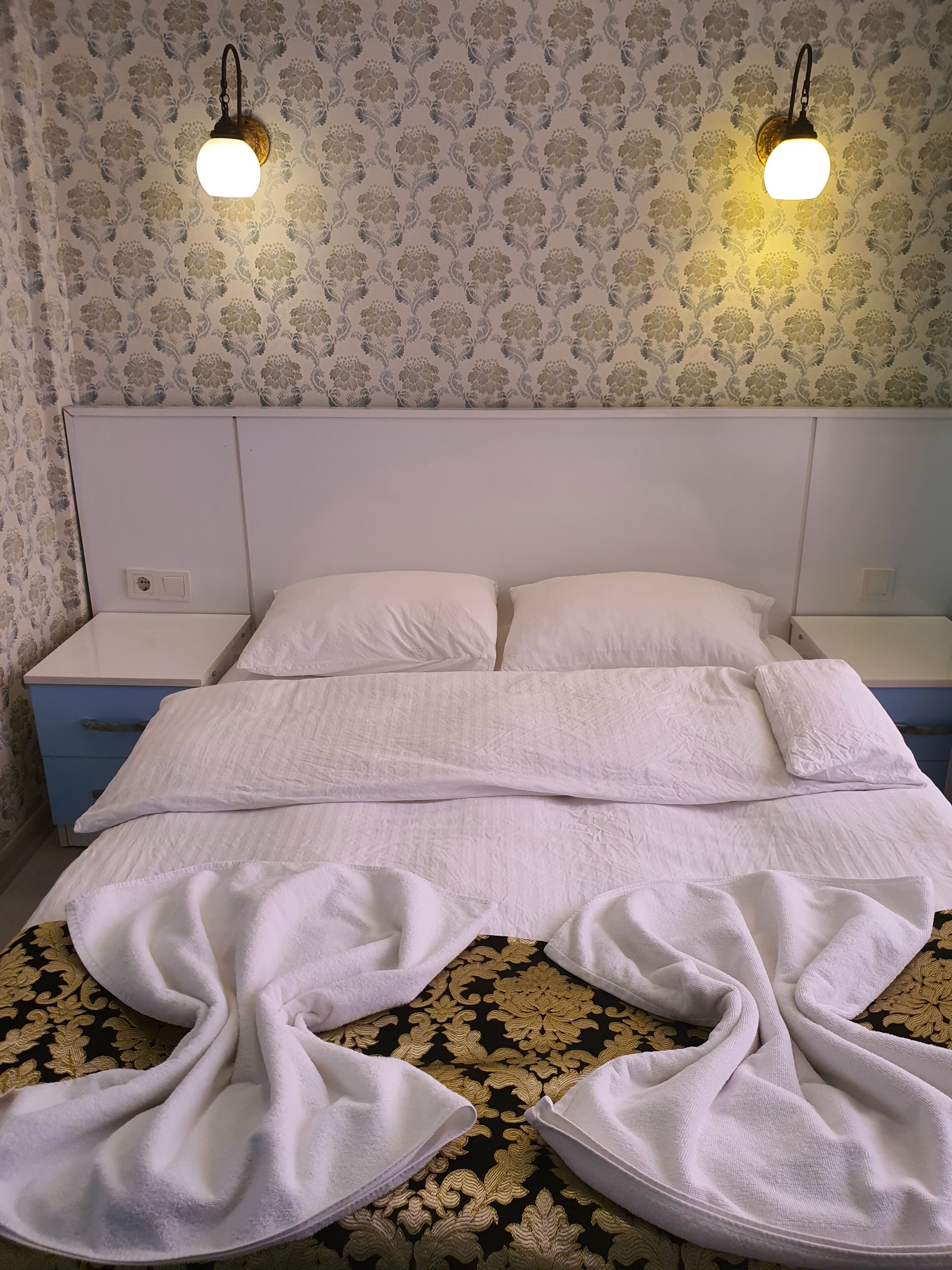 A neatly made bed with white linens, a headboard, and two bedside lamps.