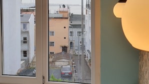 Quarto com uma grande janela com vista para a paisagem urbana, um radiador e um lustre.