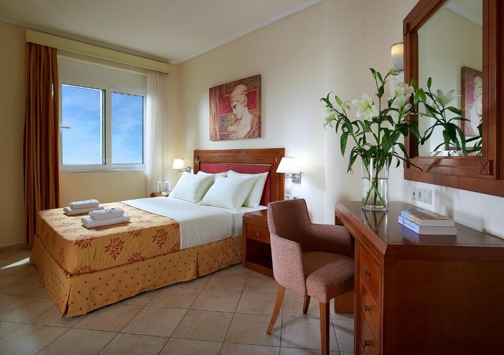 A hotel room with a bed, bedside tables, a chair, a desk, a mirror, and a window.