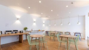 A modern dining area with wooden tables and green wire chairs, a long counter with kitchen appliances, and pendant lighting. - Hôtel Porte Mars Reims Gare Centre (Reims)