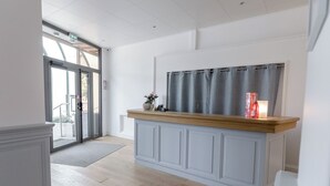 A modern interior with a wooden counter and grey cabinets, a large window with curtains, and a door leading outside. - Hôtel Porte Mars Reims Gare Centre (Reims)