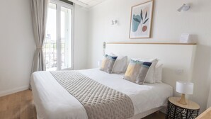 A hotel room with a large bed, a bedside table with a lamp, a window with curtains, and a wall-mounted phone. - Hôtel Porte Mars Reims Gare Centre (Reims)