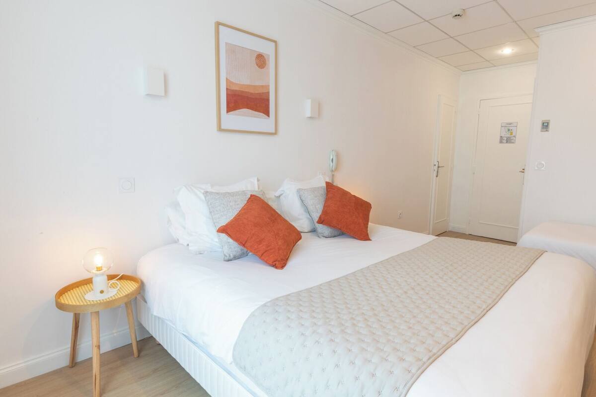 A hotel room with a bed, a bedside lamp, a framed picture on the wall, and a door in the background.