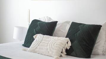 Un lit bien fait, recouvert d’un plaid vert et agrémenté de deux oreillers, un tableau abstrait encadré accroché au mur, et une table de chevet avec une lampe.