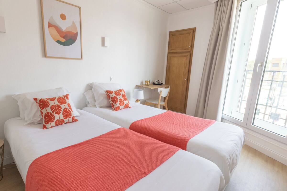 A hotel room with two beds, a desk, a chair, and a large window.