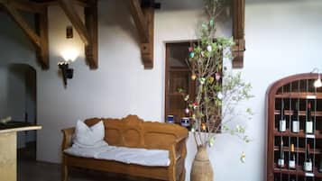 A wooden bench with a white cushion, a vase with branches and colorful ornaments, and a wine rack with bottles.