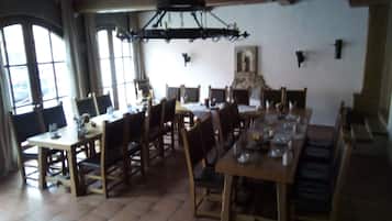 A dining area with wooden tables and chairs, a chandelier, and a stone fireplace.