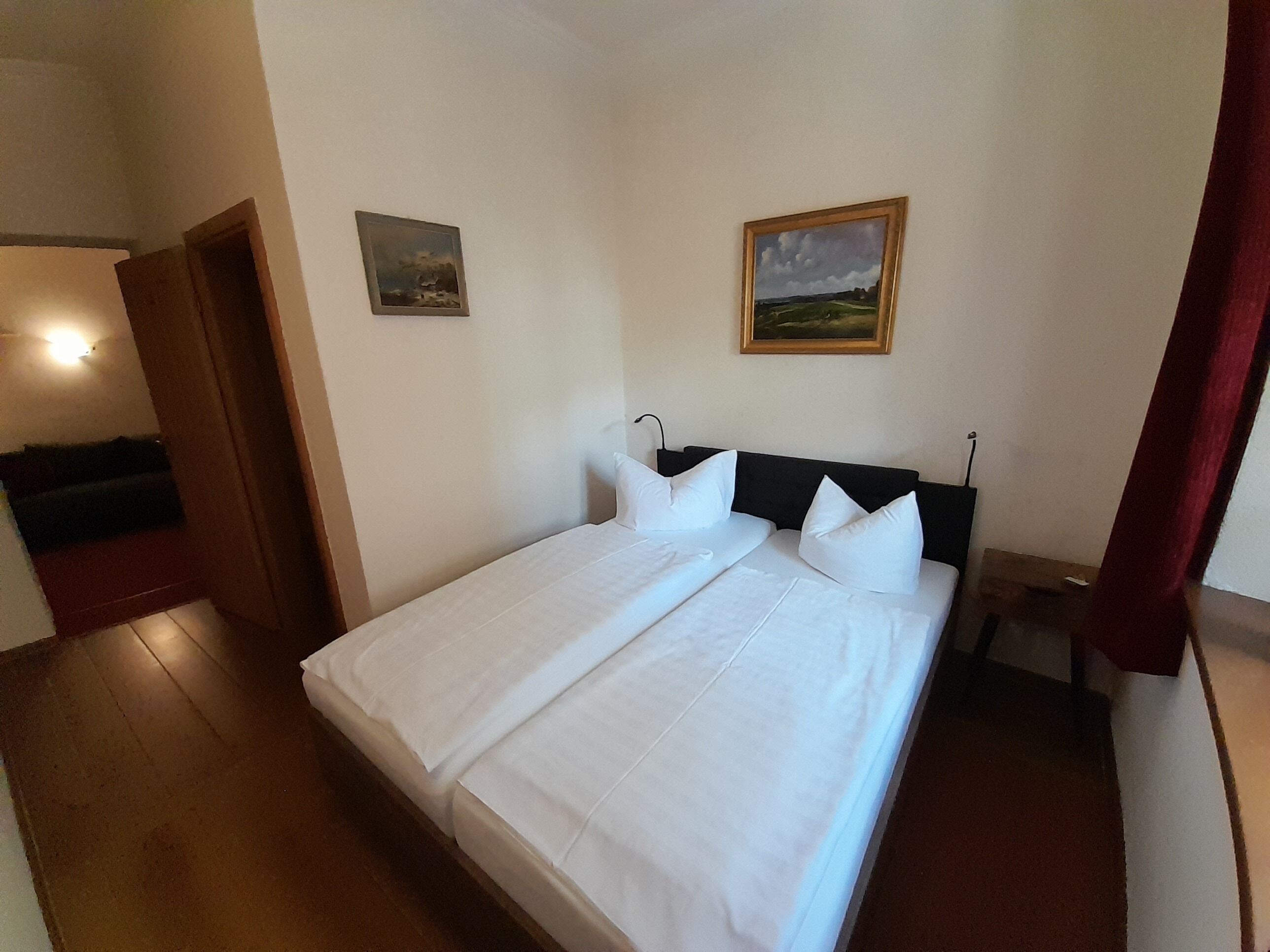 Ein Doppelbett mit weißer Bettwäsche, ein Holzkopfteil und zwei an der Wand befestigte Bilder.