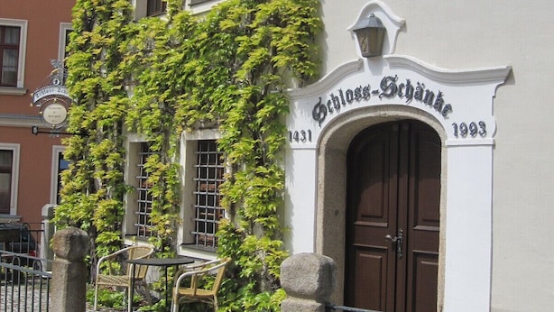 A building with a white facade, a brown door, and a sign reading "Schloss-Schank 1993".