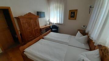 Una habitación con dos camas de madera, un escritorio, una silla, un armario, una ventana con cortinas y un cuadro colgado en la pared.