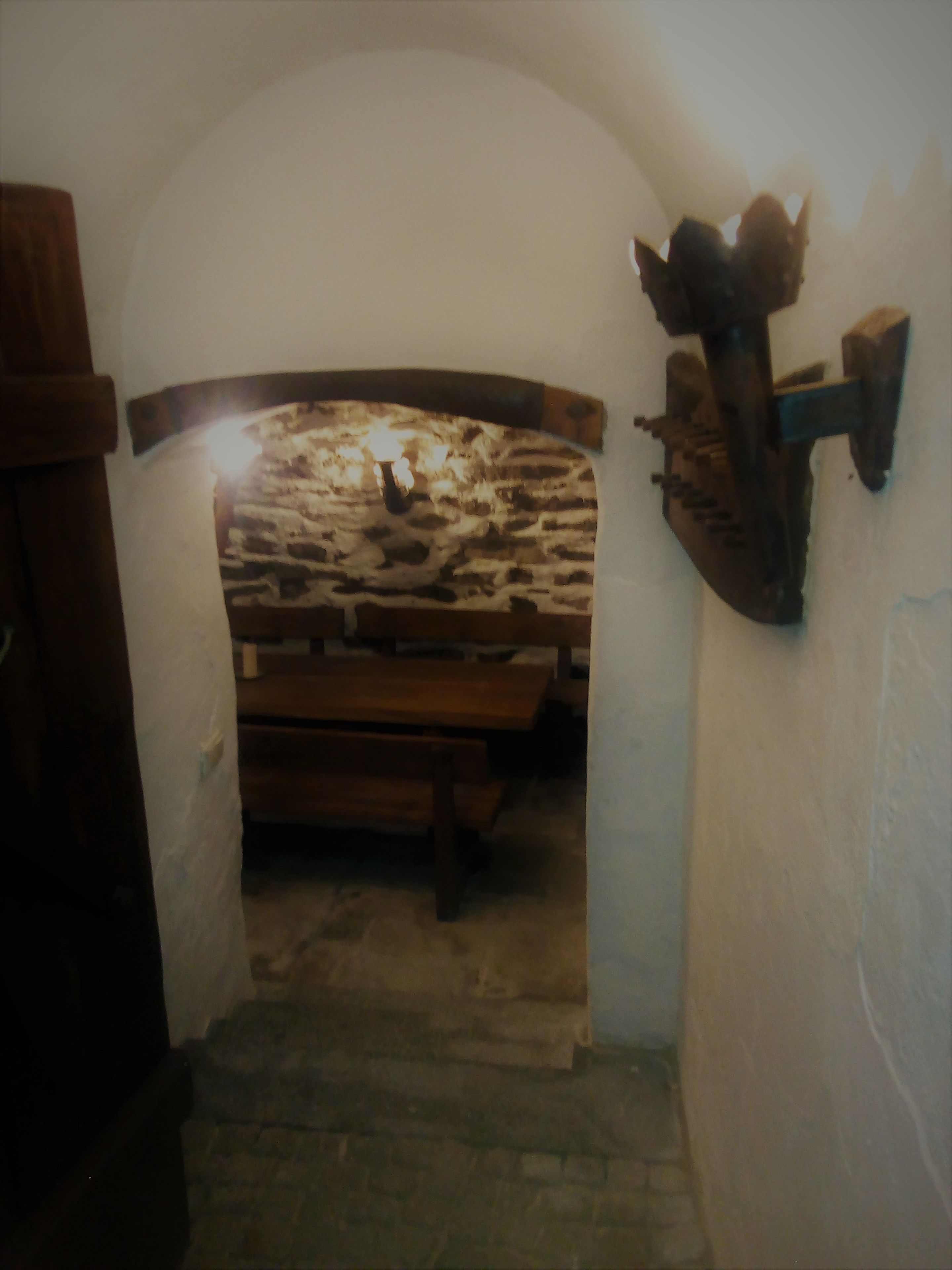 Una escalera estrecha que lleva a una zona con banco de piedra, una pared de piedra rústica y un banco de madera.
