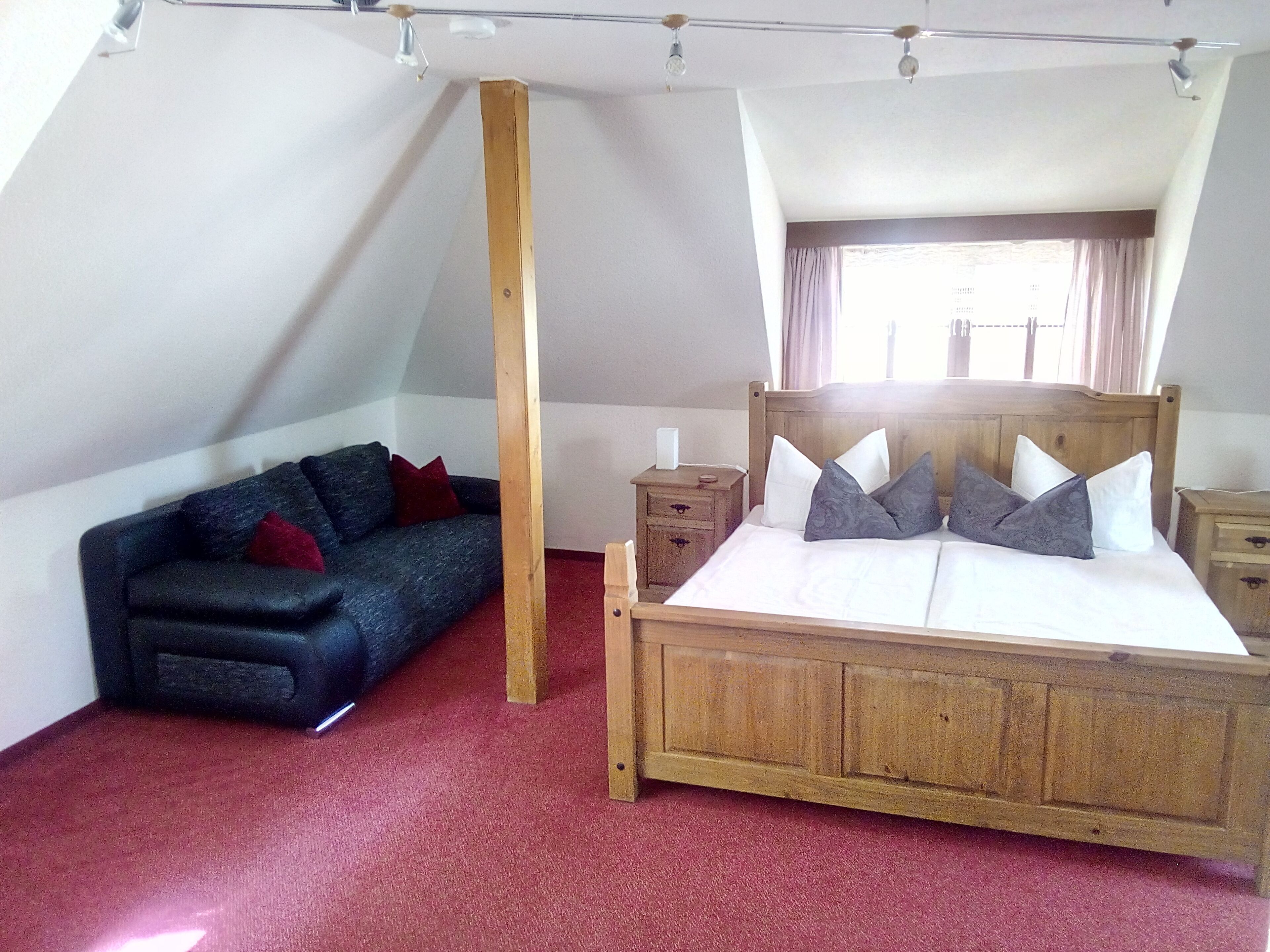 A bedroom with a wooden bed, a dark sofa, and a red carpet.