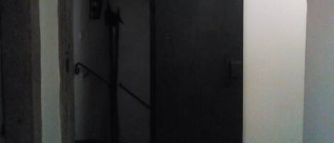 A narrow hallway with a dark door at the end, a staircase with a handrail, and a small window on the wall.
