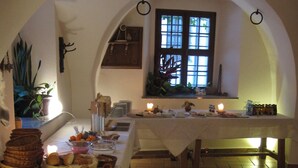 A breakfast buffet setup with various food items and utensils, a tiled floor, and a window with natural light.