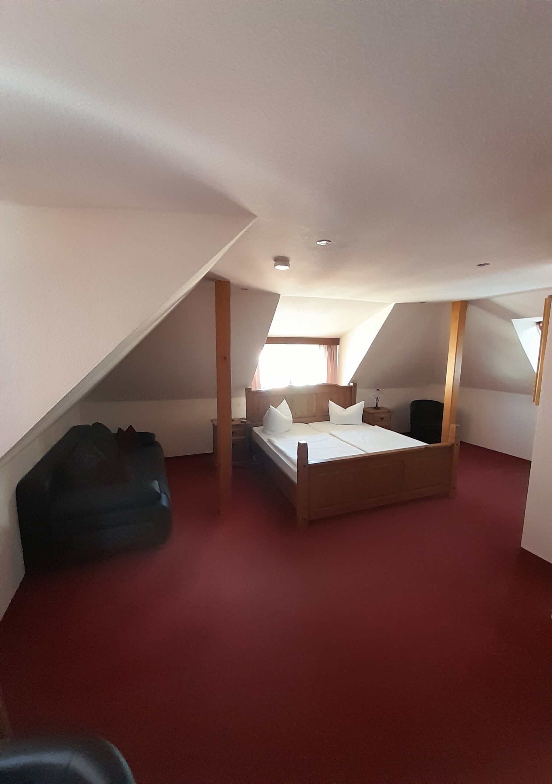 Un dormitorio con techo inclinado, una cama, una mesita de noche y una ventana.