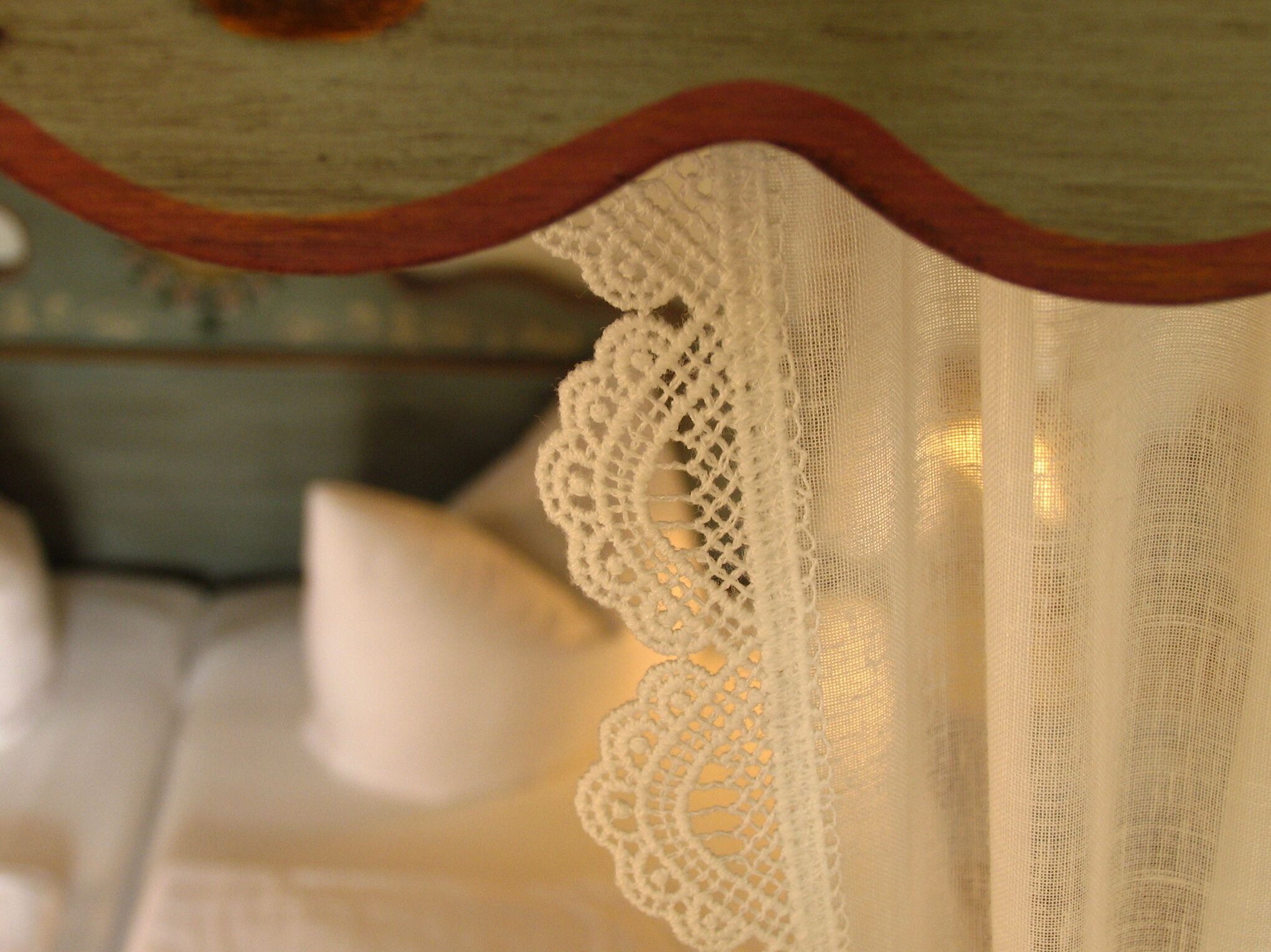 Detalle de un cortinero blanco de encaje con adornos de madera.