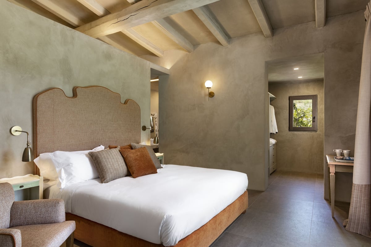 A bedroom with a large bed, a nightstand, a chair, and a window.