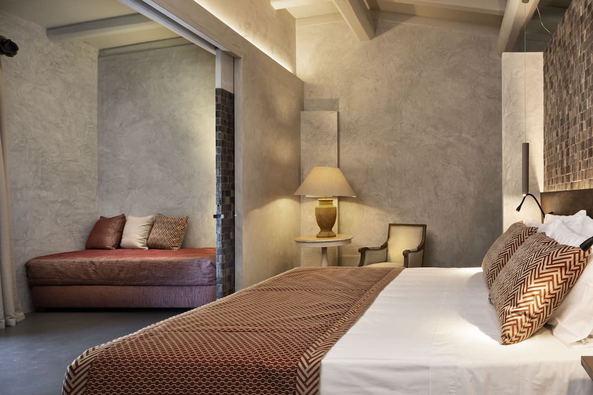 A bedroom with a bed, a sofa, a lamp, and a small table.