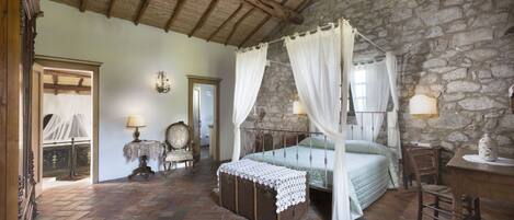 A bedroom with a stone wall, wooden ceiling, and a four-poster bed with a canopy.