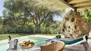 Zona junto a la piscina con mesa lista para comer, una silla de descanso y una gran formación rocosa.