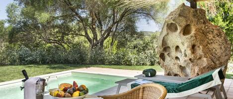 Zona junto a la piscina con mesa lista para comer, una silla de descanso y una gran formación rocosa.