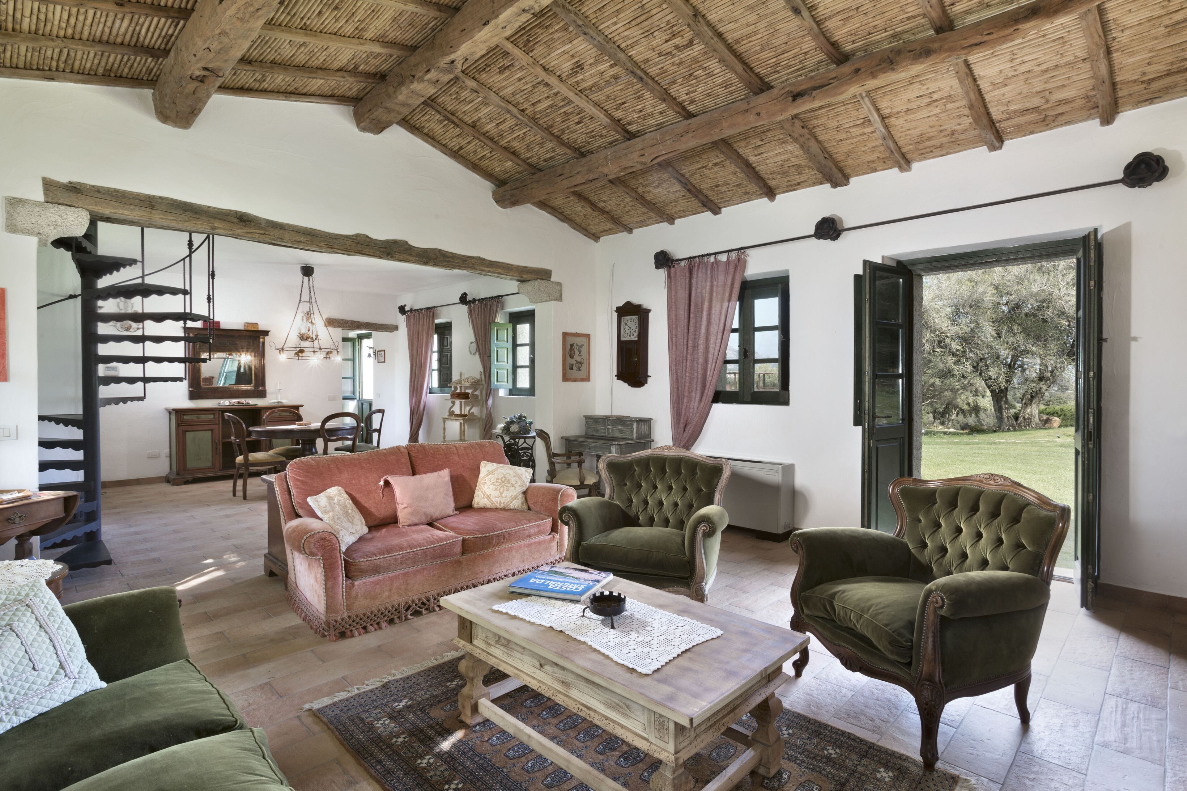 Uma sala de estar ampla com teto de madeira, uma poltrona verde, um sofá vermelho e um espaço de jantar ao fundo.
