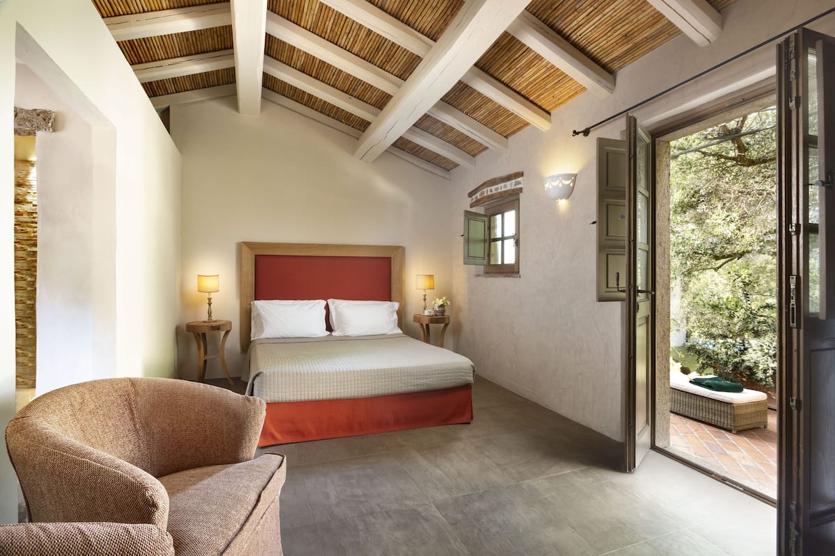 A bedroom with a bed, two bedside lamps, a chair, and a view of an outdoor area through a glass door.