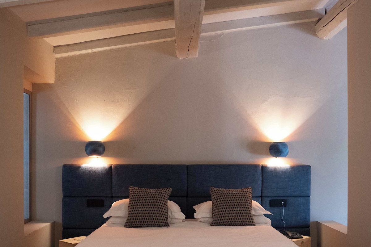 A modern hotel room with a large bed, two bedside tables, and wall-mounted lights.