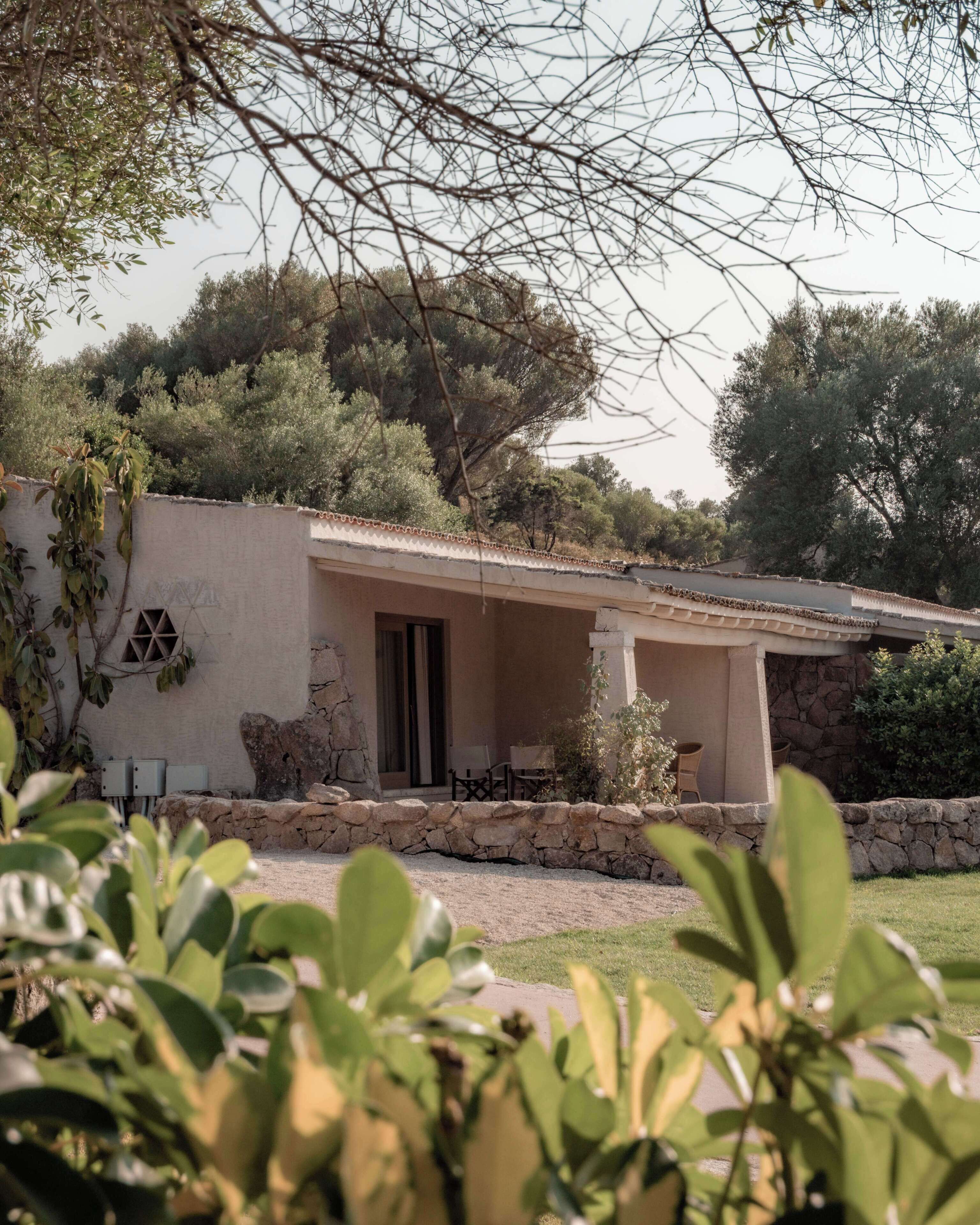 Una casa con muro de piedra, un porche cubierto y un jardín.