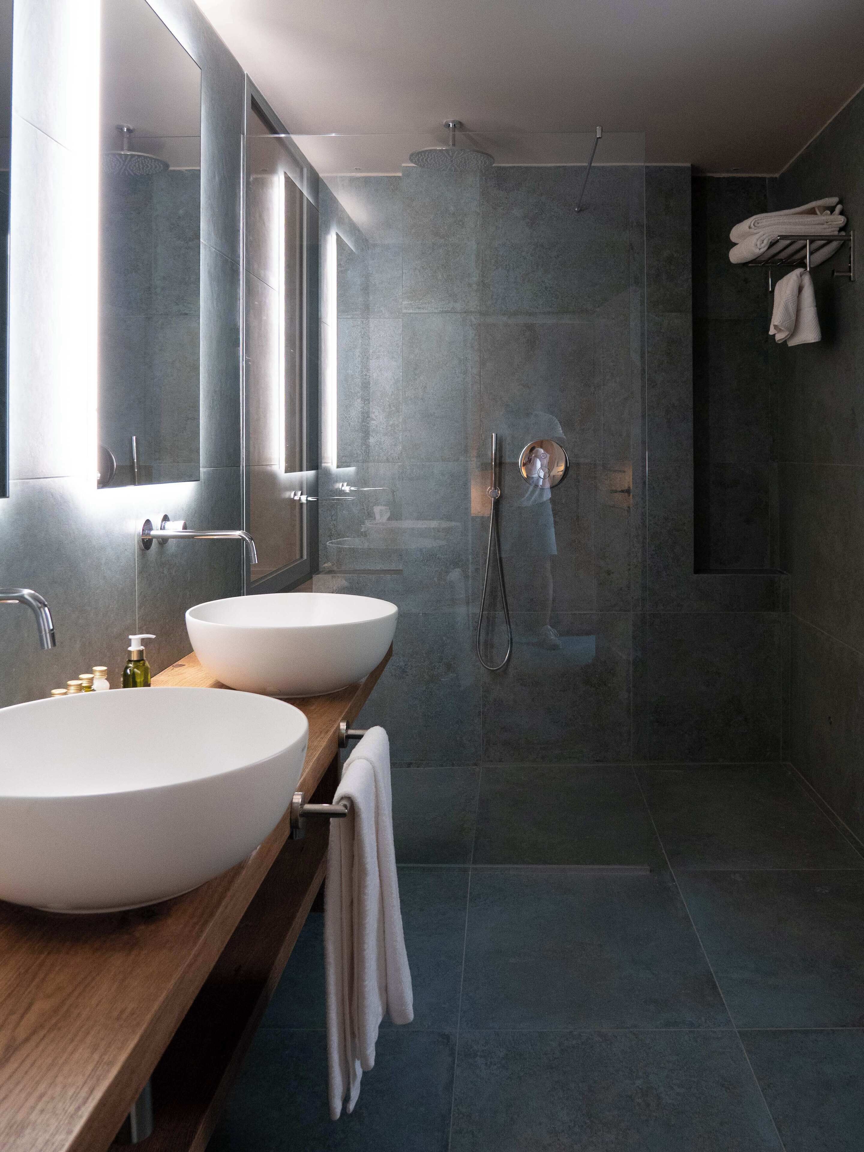 Une salle de bain moderne avec deux grands lavabos blancs, un meuble-lavabo en bois, un grand miroir et une cabine de douche en verre.