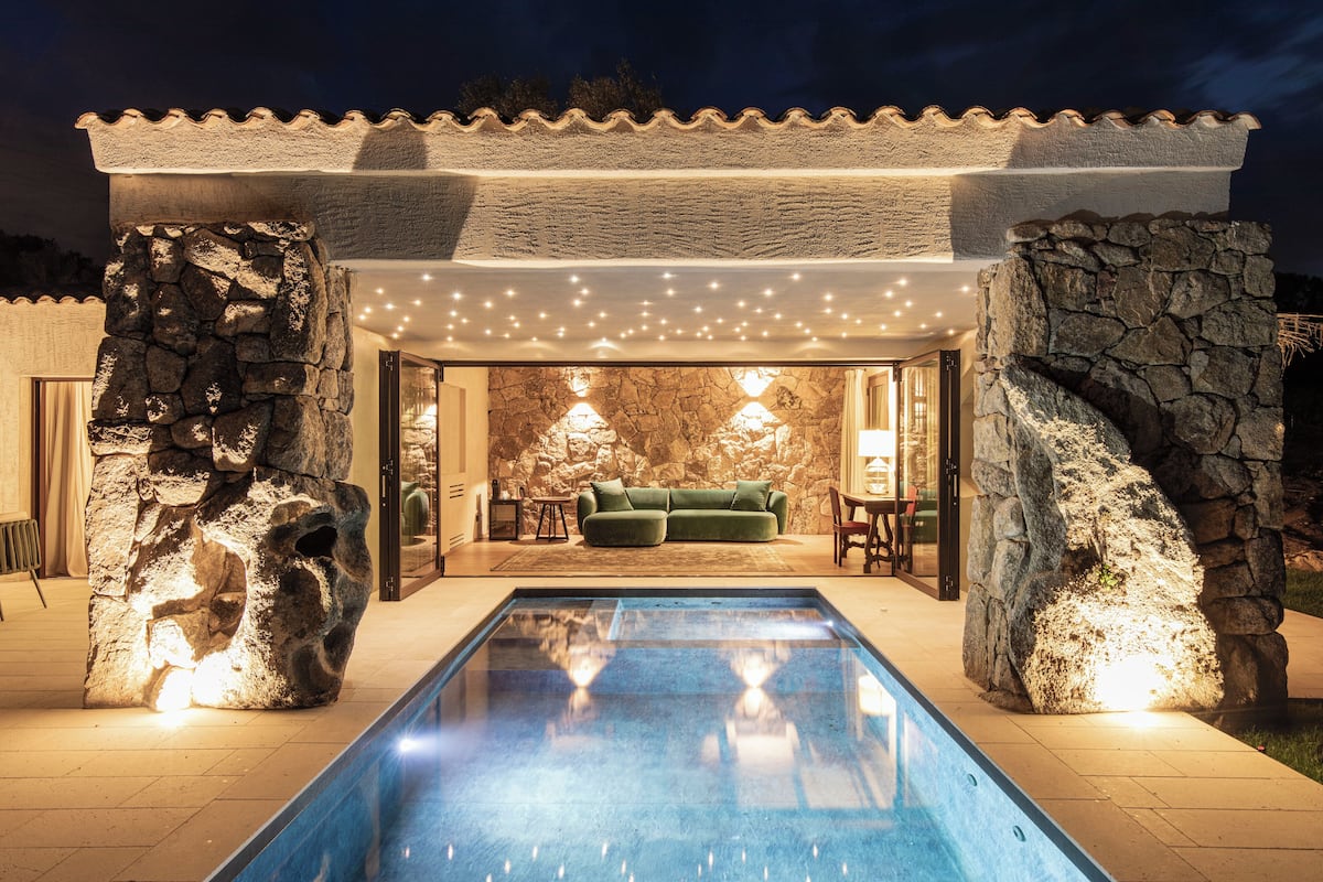 A pool area with a stone wall, a green sofa, and string lights.