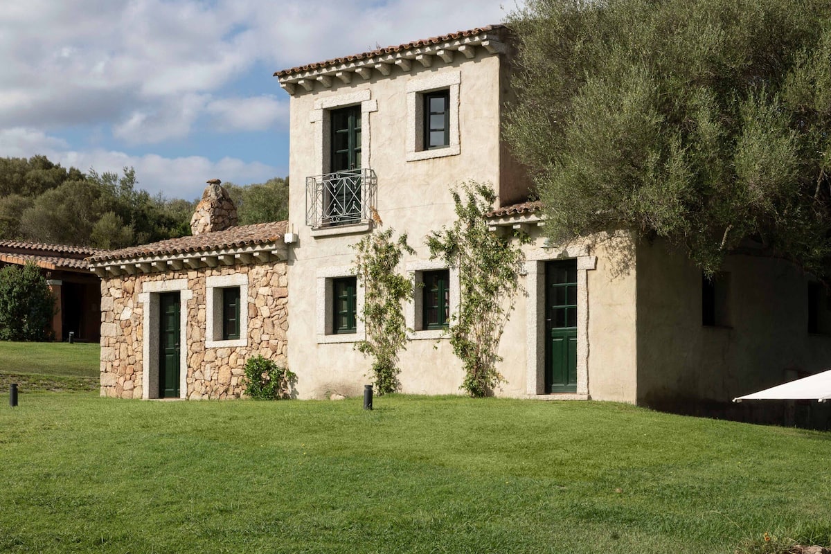 A two-story building with a stone facade, green shutters, and a tiled roof.