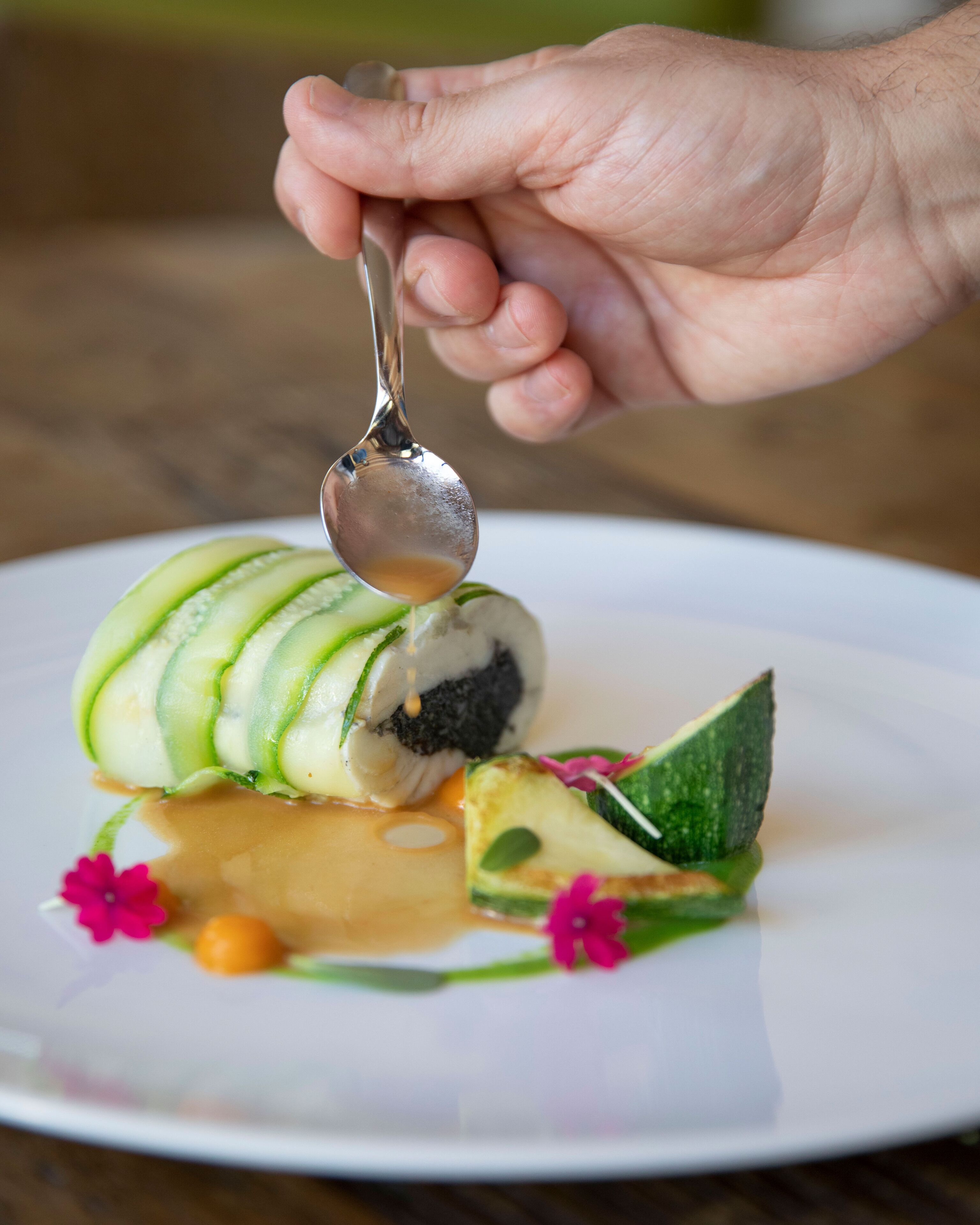 A hand holding a spoon over a dessert on a white plate.