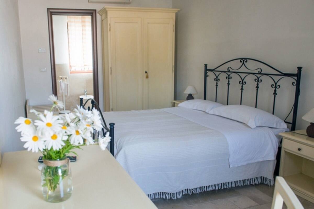 A bedroom with a bed, a nightstand, a dresser, a mirror, and a vase of flowers on a table.